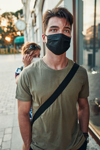 Young man walking along a store front in the city center in the evening wearing the face mask
