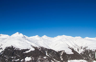 Low angle view of snowcapped mountains against clear blue sky