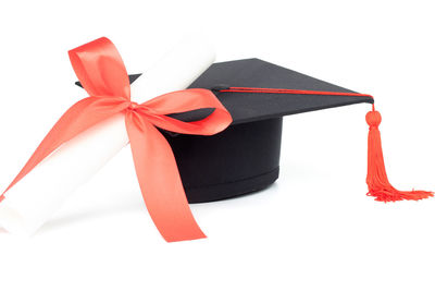 Close-up of mortarboard and certificate against white background