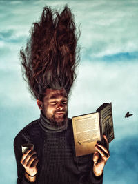 Portrait of smiling young man holding book against sky