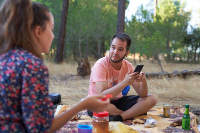 Man using smart phone while sitting in forest during picnic