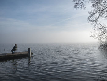 Full length of man sitting on pier by sea against sky