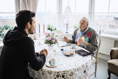 Senior man communicating to caretaker at dining table in nursing home