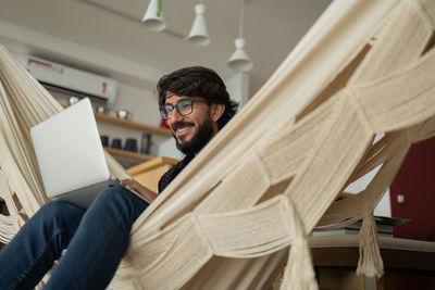 Young man  black glasses working with laptop on a white hammock notebook for working. home office