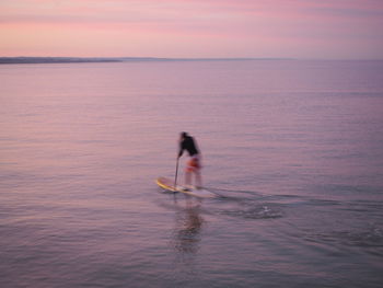 Man in sea against sky during sunset