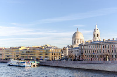 View of buildings by river against sky in city