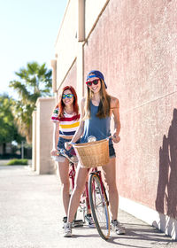 Portrait of happy female friends on tandem bicycle at sidewalk against wall
