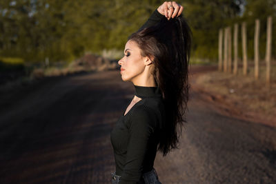 Side view of young woman with hand in hair standing on road