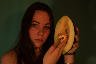 Portrait of young woman holding melon against wall