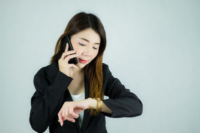 Young woman using phone while standing against white background