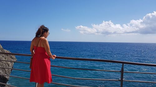 Woman looking at sea while standing by railing against sky