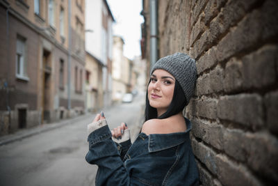 Side view portrait of young woman standing by brick wall in city