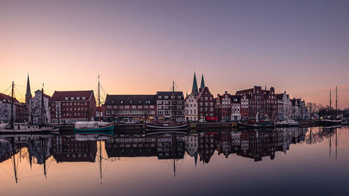 Sailboats in river by buildings against sky during sunset