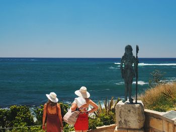 Rear view of people standing by sea against clear sky