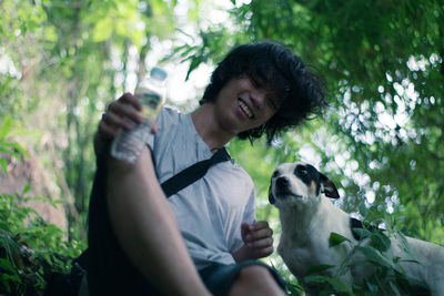 Low angle view of young man sitting with dog at forest