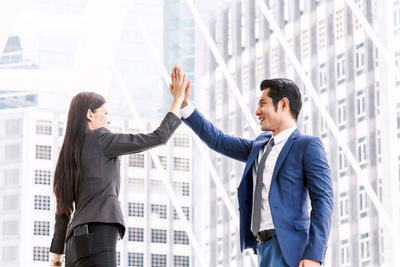 Colleagues giving high-five while standing against buildings in city