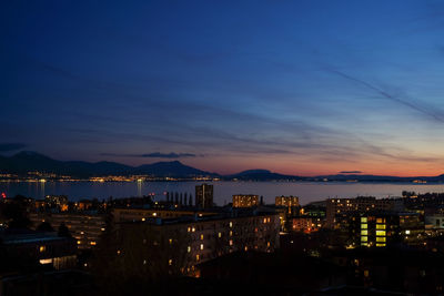 Illuminated cityscape by sea against sky at night