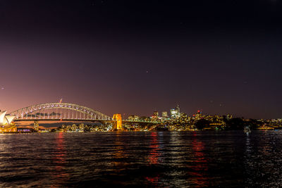 Illuminated bridge over river against sky at night