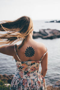 Rear view of woman with tousled hair standing at beach