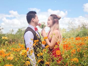 Young couple kissing and flowers on land against sky