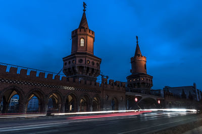 Light trails on road by building against blue sky