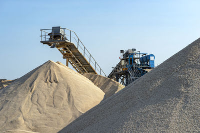 Conveyor belt over heaps of gravel against the blue sky at an industrial cement plant.