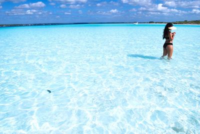 Side view of woman with bikini standing in blue sea