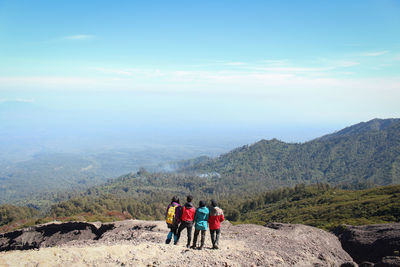 Rear view of friends looking at view while standing on mountain against sky during sunny day