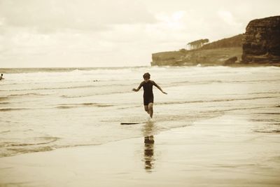 Rear view of man standing on beach against sky