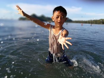 Portrait of boy standing in sea against sky during sunny day