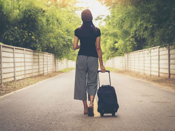 Full length of woman with luggage walking on road against trees