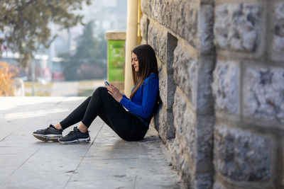 Teen girl sitting on the floor, talking on mobile smart phone, texting and surfing the net