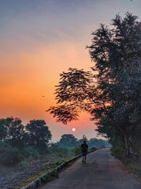 Rear view of man walking on road against sky during sunset