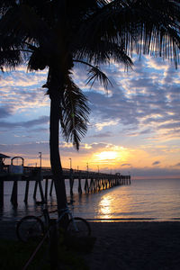 Silhouette palm trees by swimming pool against sky at sunset