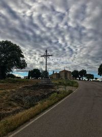 Road amidst field and buildings against sky