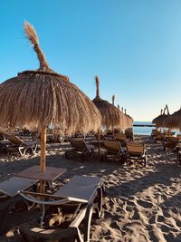 Lounge chairs and parasols on beach against clear sky