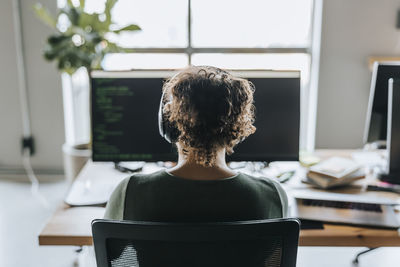 Rear view of female programmer with curly hair wearing headphones working in office