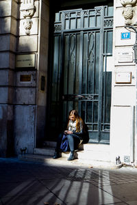 Full length of woman sitting outside building