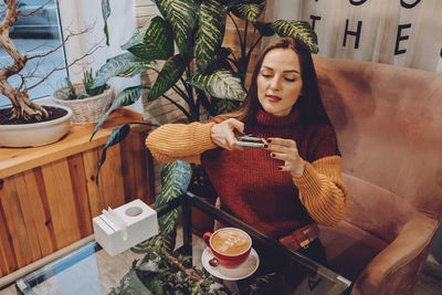 High angel view of woman sitting by coffee cup at home