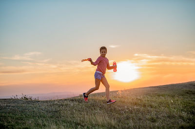 Girl running on field against sky during sunset