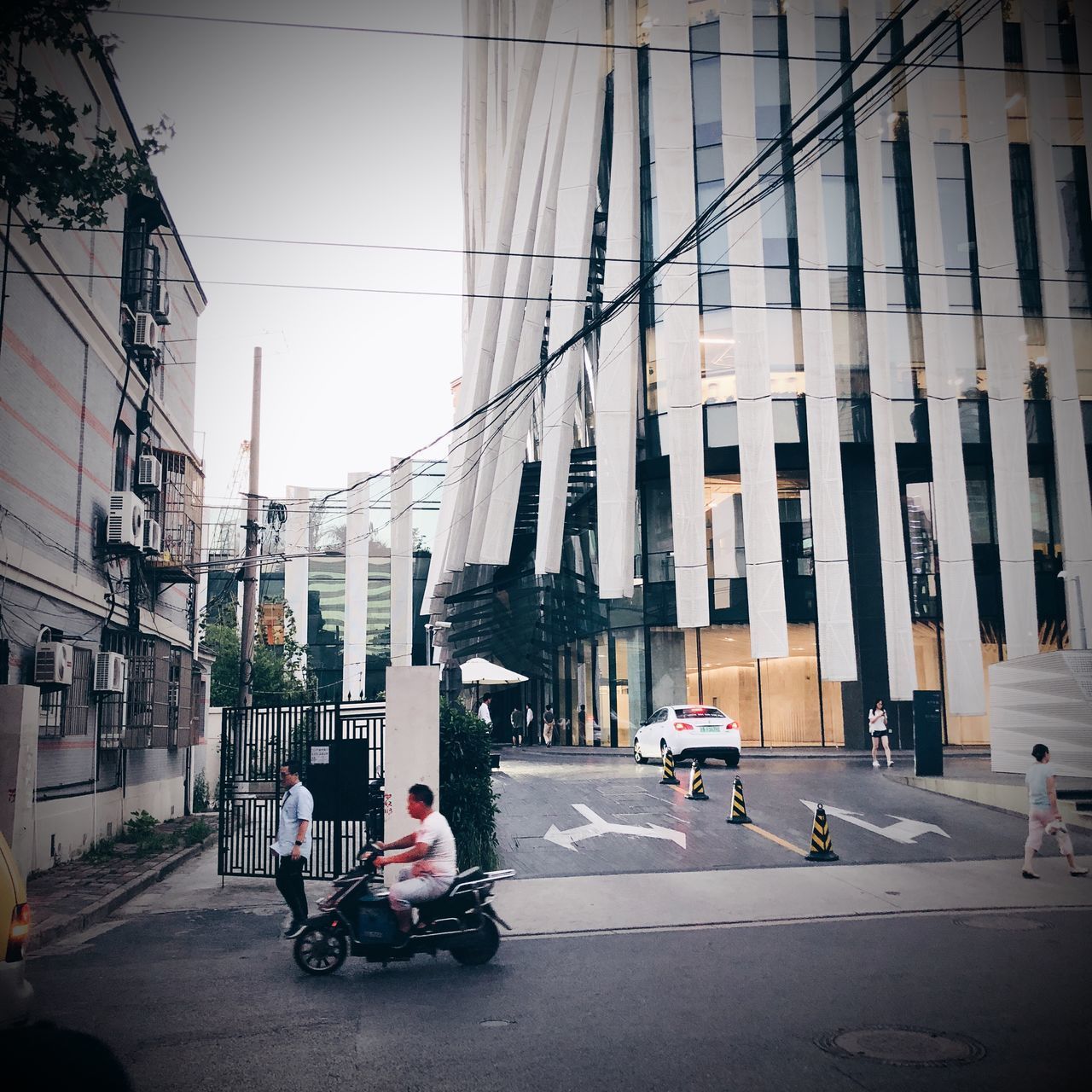 MAN RIDING MOTOR SCOOTER ON ROAD BY BUILDINGS