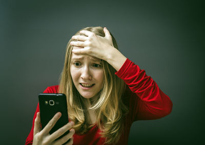Close-up of worried young woman using phone against gray background