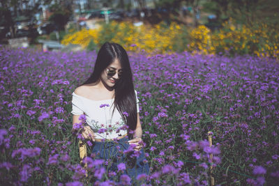 Beautiful woman standing by purple flowering plants on field