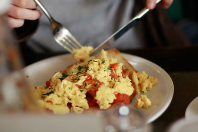 Midsection of person having scrambled eggs in plate on table