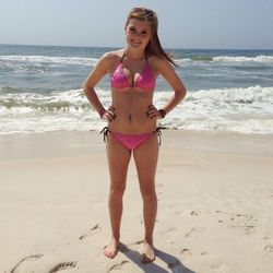 Full length portrait of smiling young woman in bikini standing on shore at beach