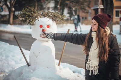 Smiling woman touching snowman in city