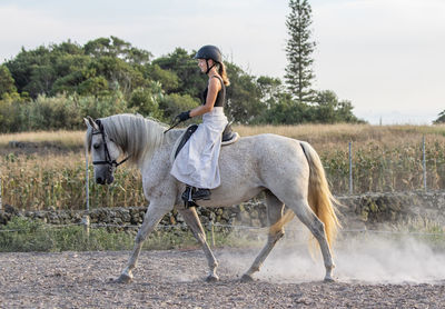 White lusitano mare, female dressage rider, outdoors on sand.