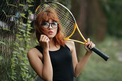 Portrait of young woman wearing sunglasses standing outdoors and playing tennis