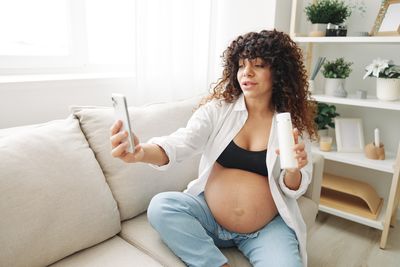 Young woman using mobile phone while lying on sofa at home