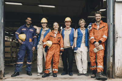 Portrait of smiling male and female workers in workwear at entrance of warehouse